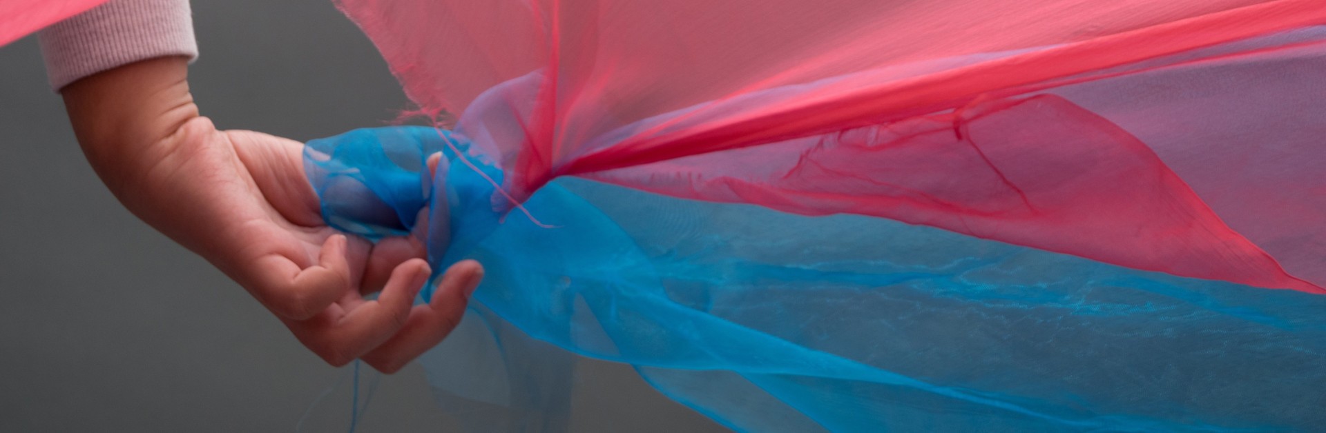 Main d'un enfant tenant deux tissus flottant au vent