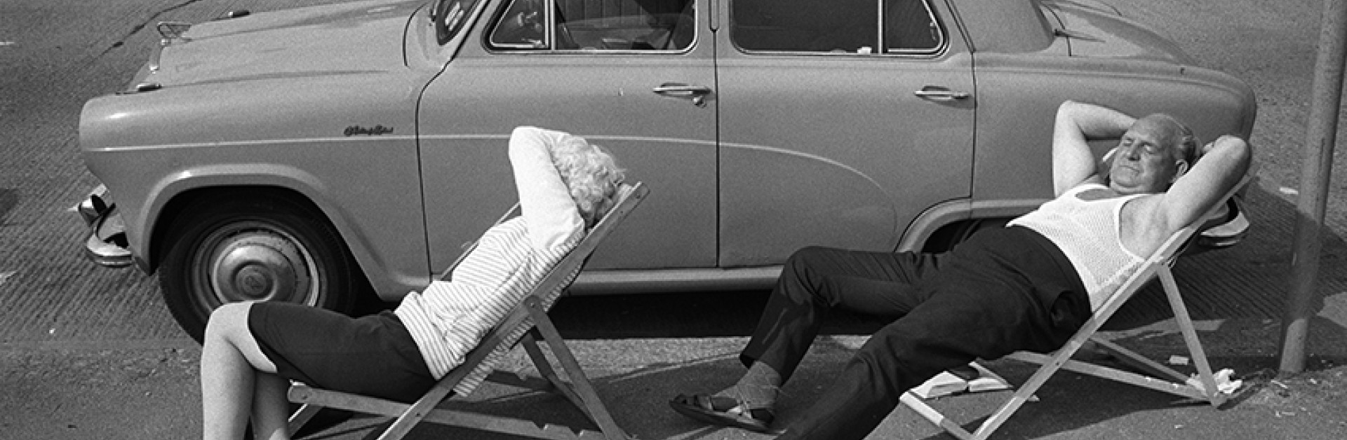 Sur un trottoir, un couple âgé dort sur des chaises longues 