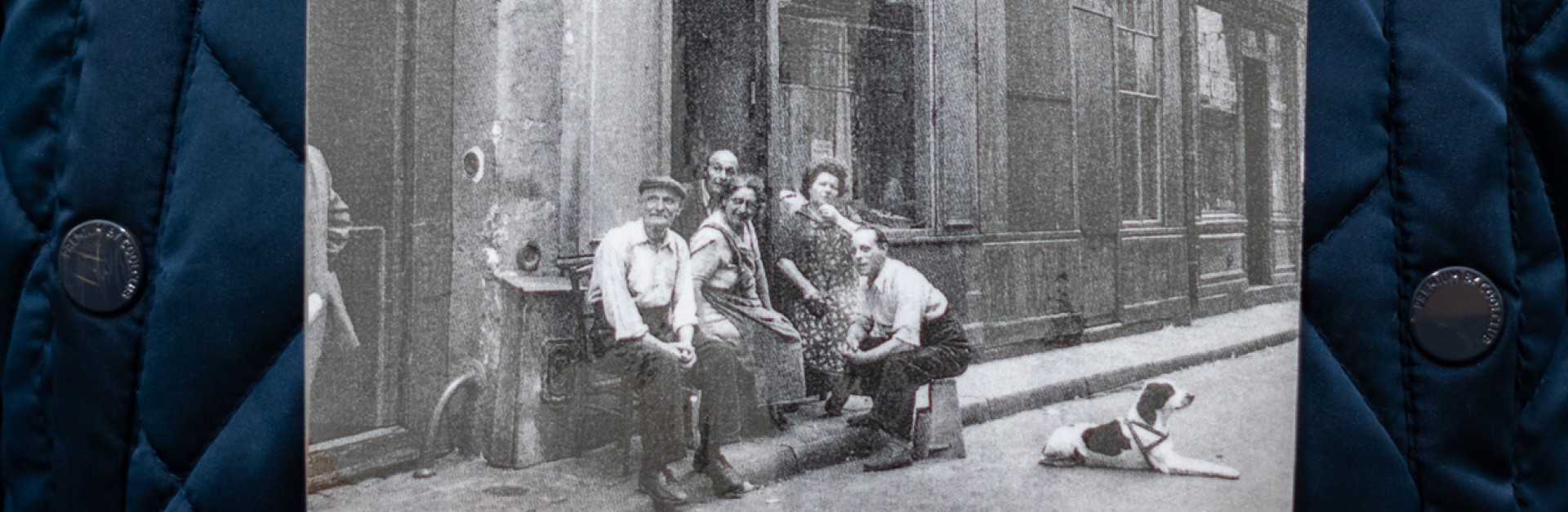 Enfant tient dans ses mains une photographie prise par Robert Doisneau. Une photo avec des adultes assis devant leur boutique