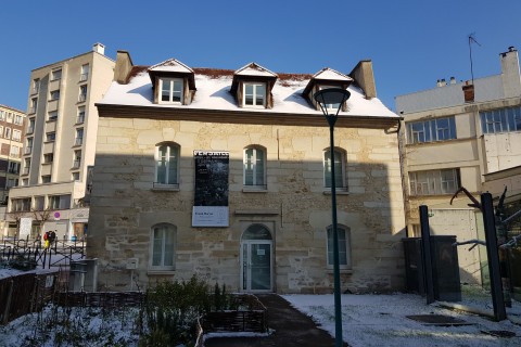 Une maison en pierre beige au toit recouvert de neige, avec une affiche devant et l